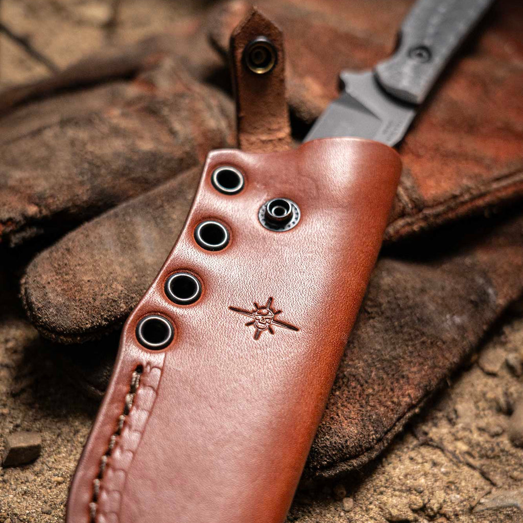 Brown leather knife sheath with black stitching on a textured surface